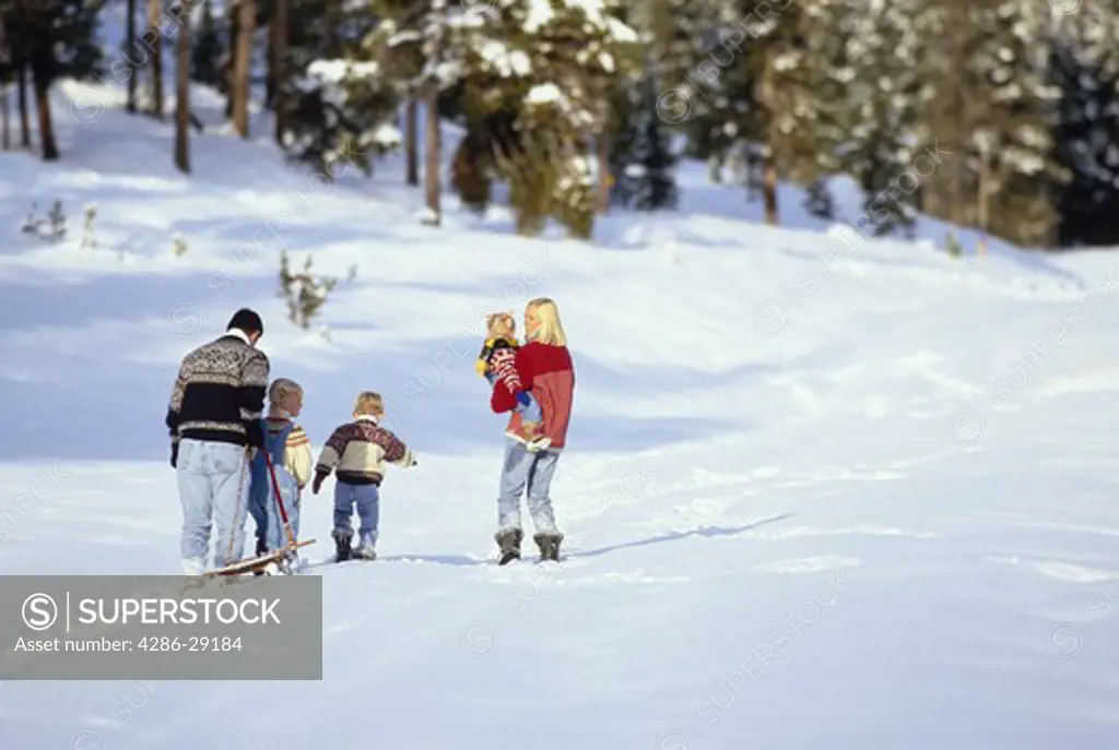 A father pulls a sled as he follows his wife and their three children across a snowy field.