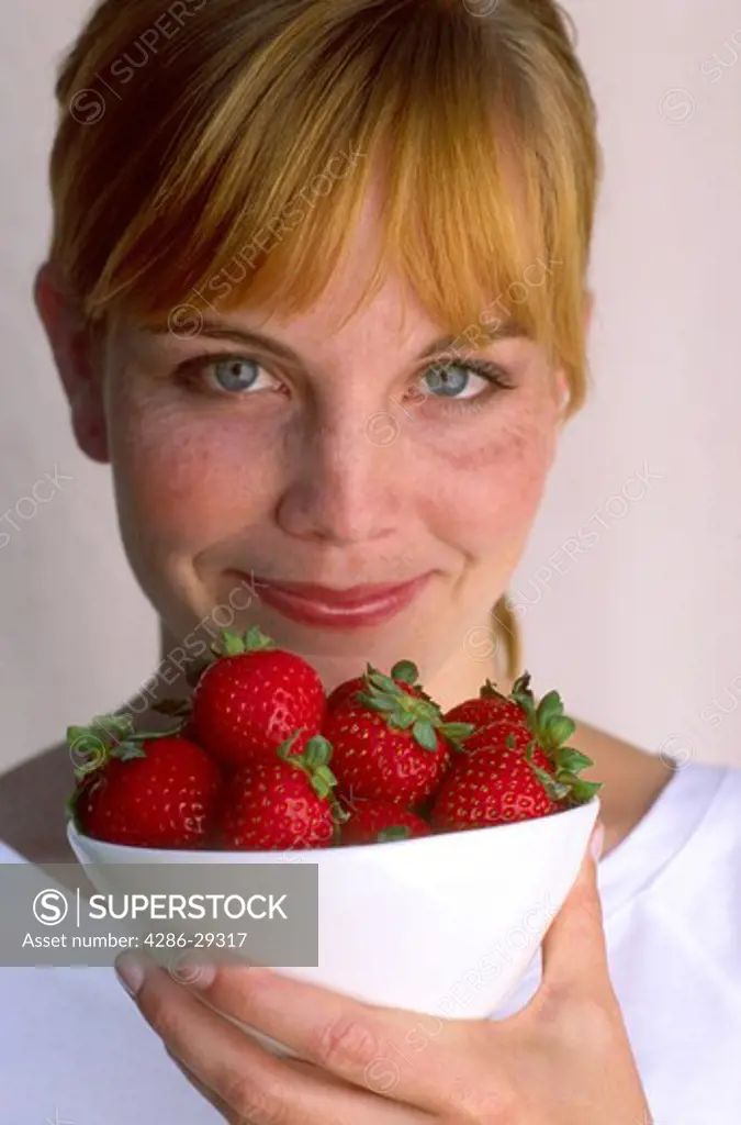Young redheaded woman with bowl of fresh strawberries
