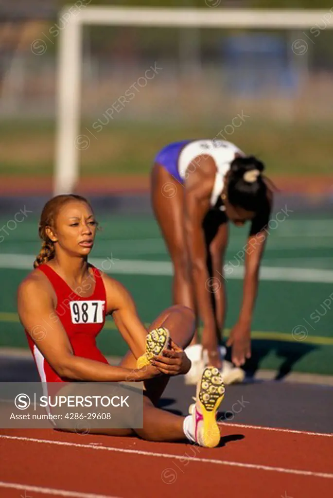 Two African-American women track runners stretch before the start of a race.