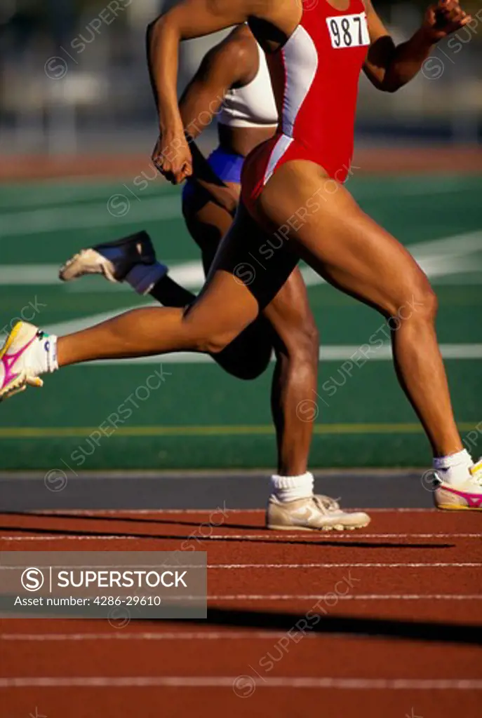Two women sprinters seen from the shoulders down as they run down the track during a race.