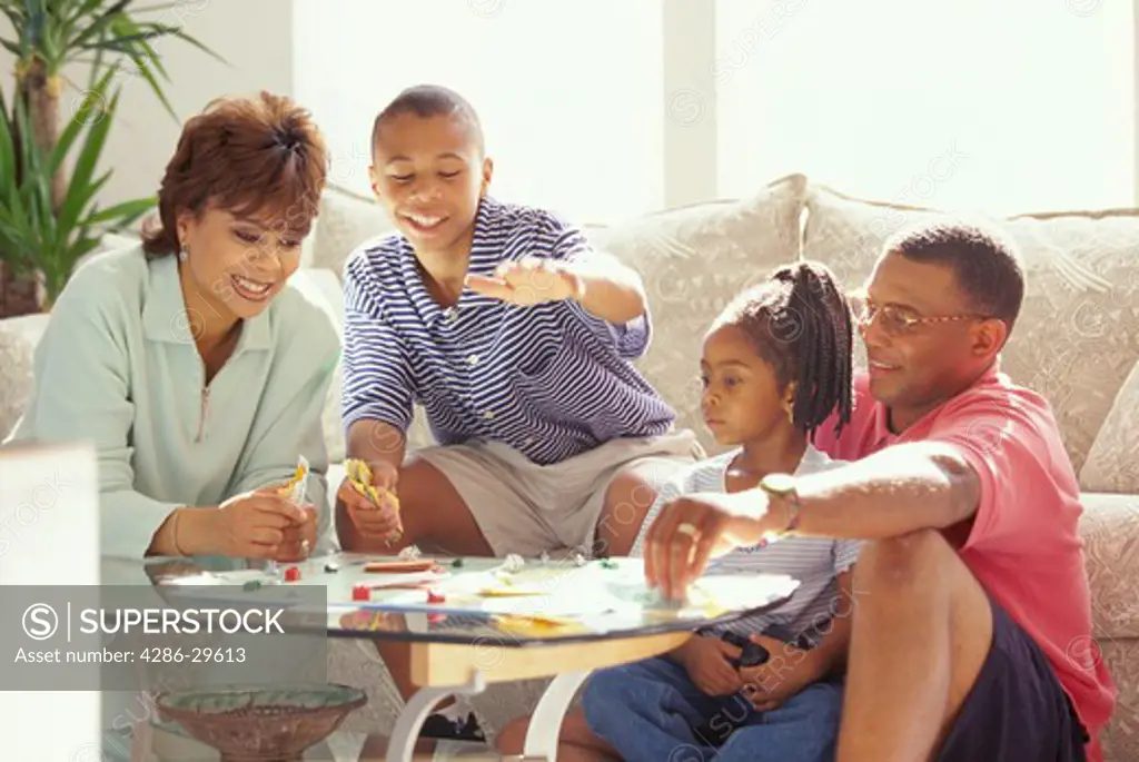 African-American family sitting around a coffee table playing a game of Monopoly.