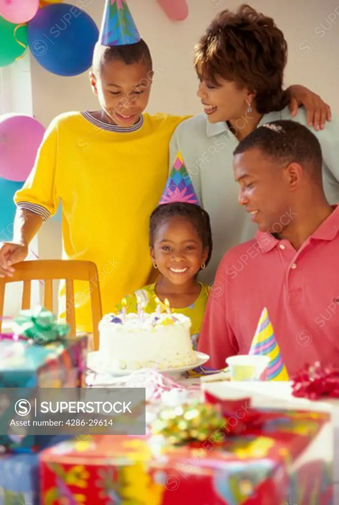African-American family gathers around a cake and presents to celebrate the daughter's birthday.