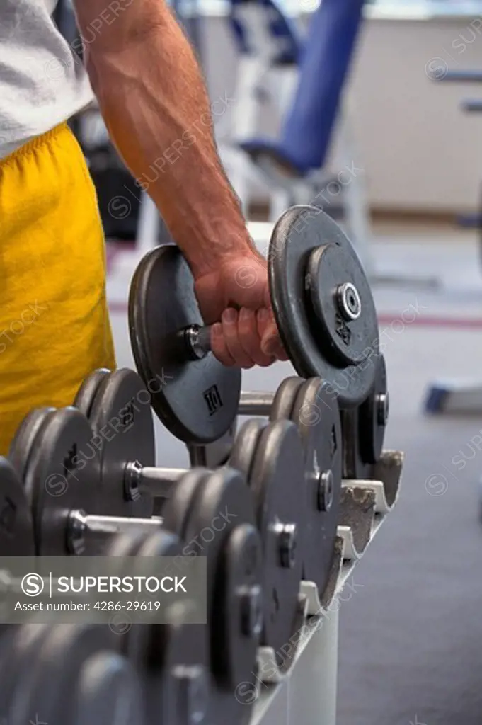 Close-up of a man's arm as he lifts a hand weight from a rack of weights.