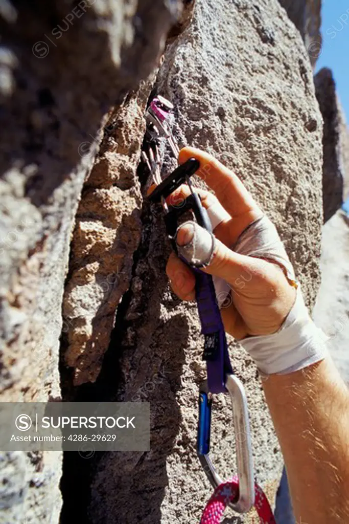 Close-up of a rock-climber's hand as he attaches a safety piton into a crack in the rockface.