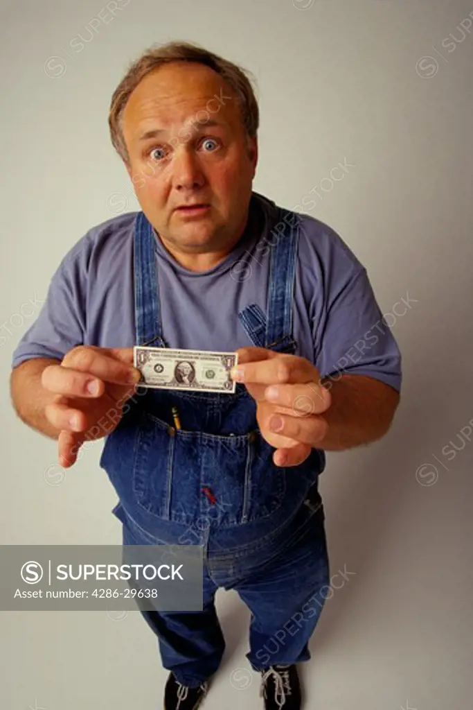 Studio shot of a surprised man wearing overalls and holding a shrunken one dollar bill.