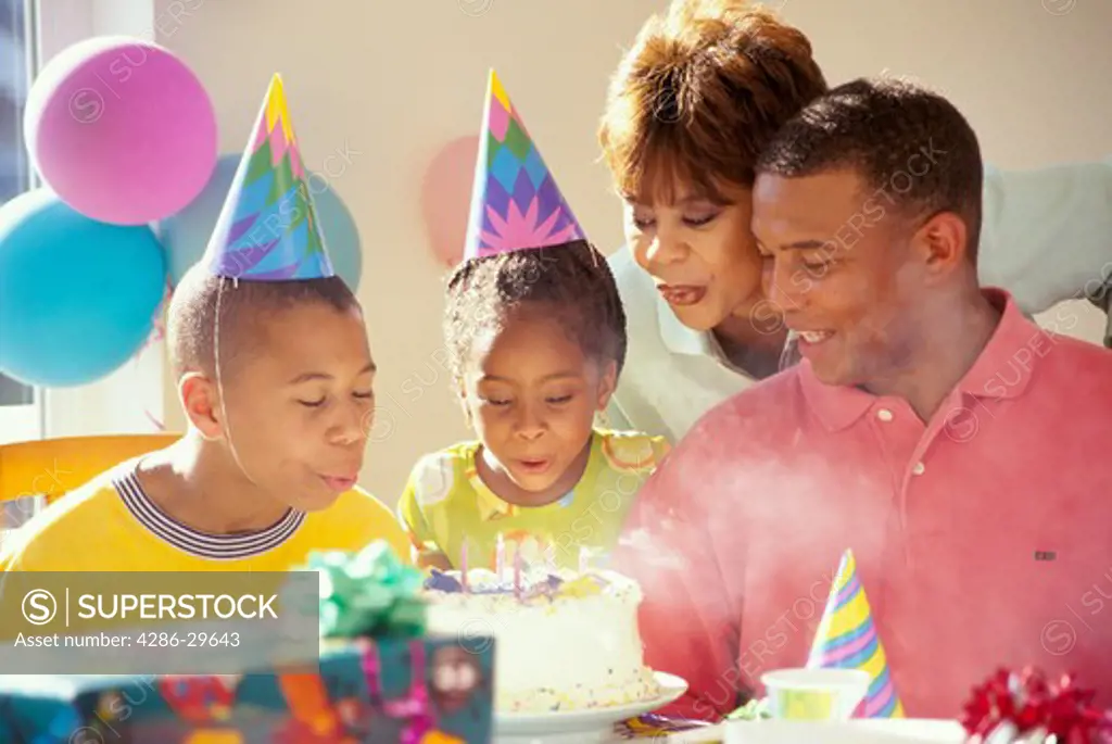 African-American family celebrating their son's birthday as both he and his sister blow out the candles. 