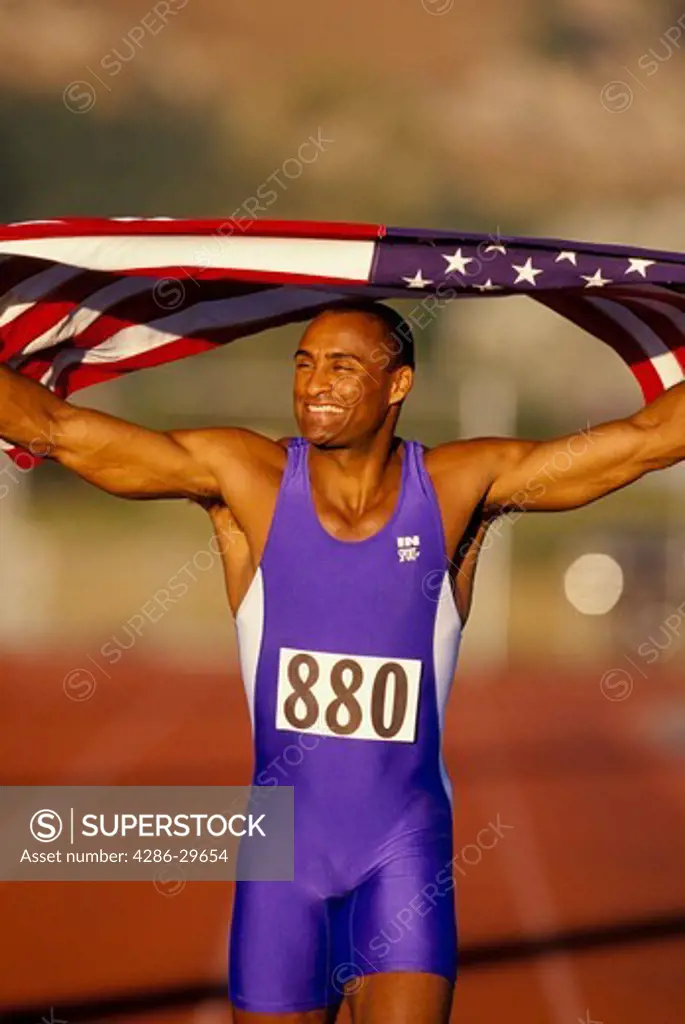 African-American man running a victory lap after a successful track event and holding the American flag over his shoulders. 
