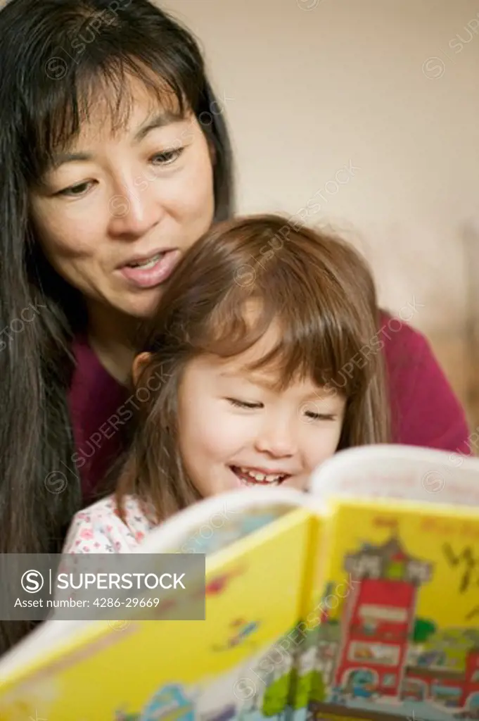 Close-up of mother  reading a book to her young daughter both of Asian ethnicity. 