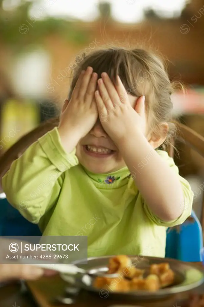 Close-up of a child covering her eyes as she is about to be spoon fed.