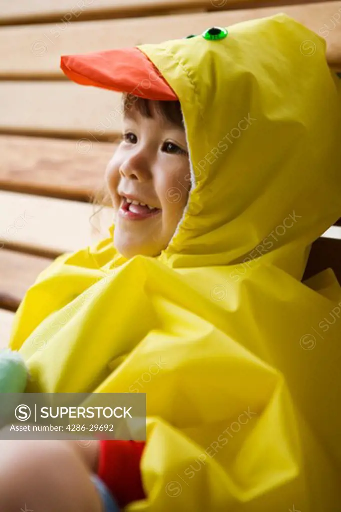 Closeup of young Asian-American girl wearing cute yellow duckie raincoat with hood.