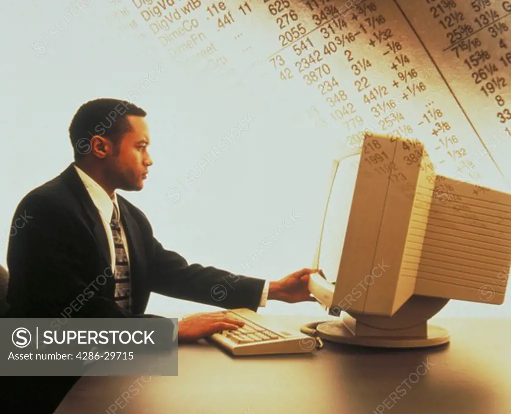 African American businessman using computer with stock quotes in background.