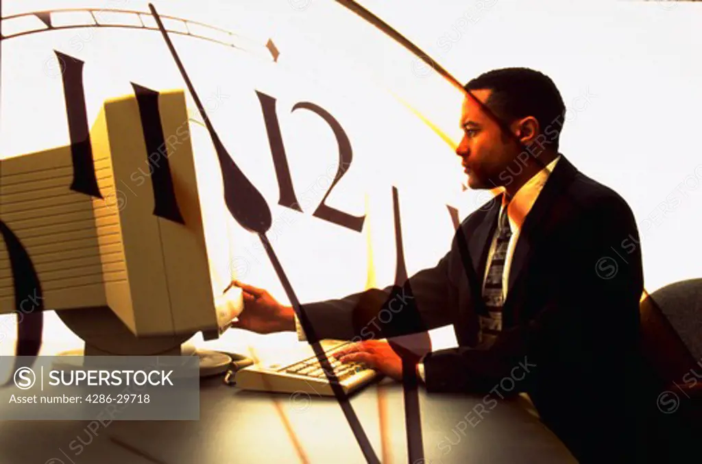 African American businessman using computer with clock in background.