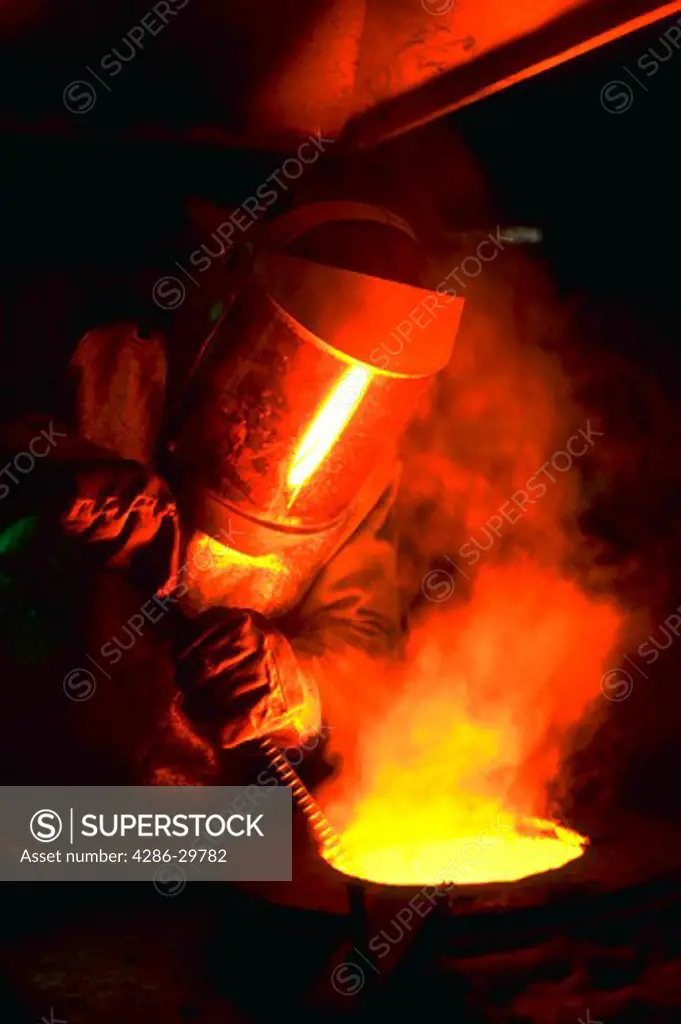 A foundry worker with a mask handling molten steel in a cauldron.