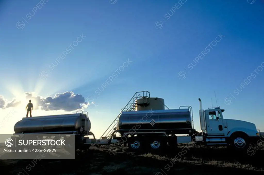 An 18-wheeler oil tanker truck with sunbeams through dark clouds.