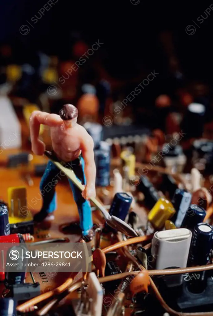 A small toy figure of a shoveling man sits amidst various transistors, resistors and other electronic parts. 