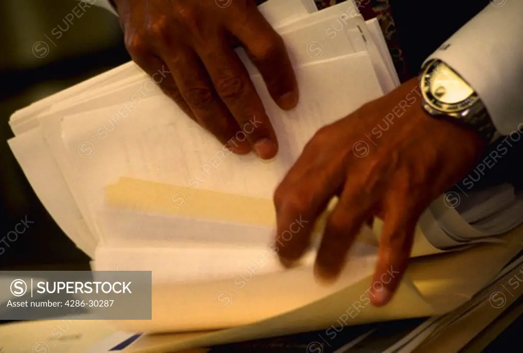 Hands of African American businessman sorting through papers.