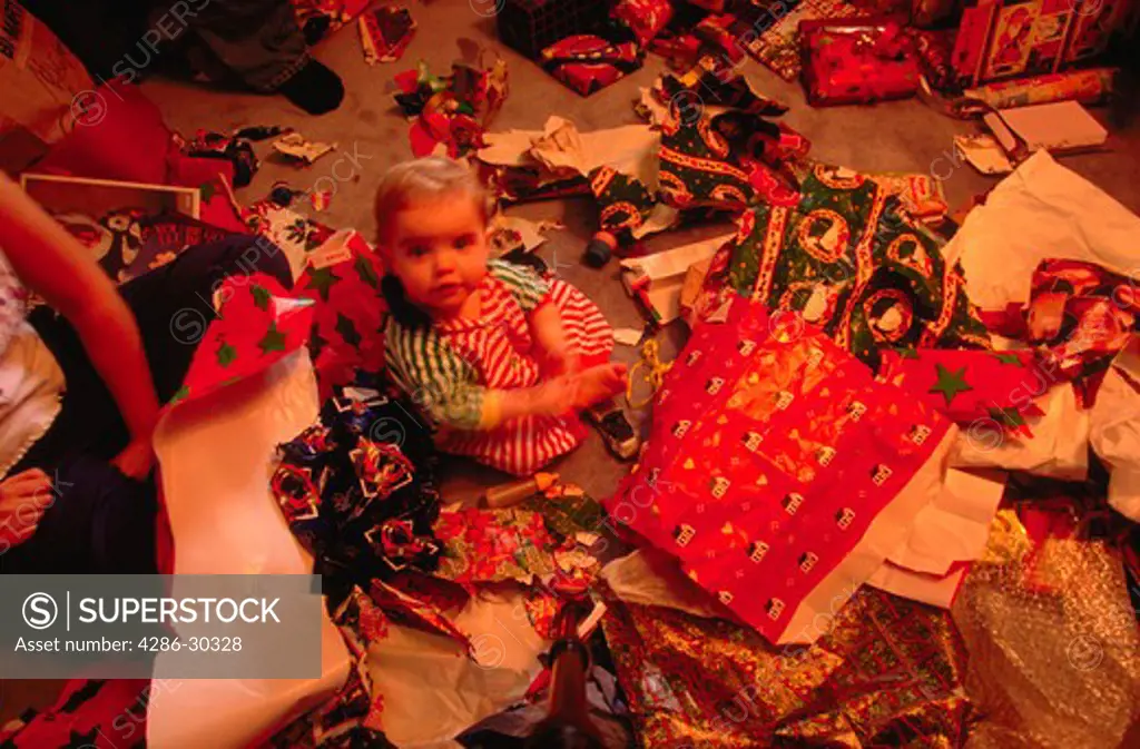 Overhead view of a young child sitting amidst the torn wrapping paper on the floor on Christmas morning.