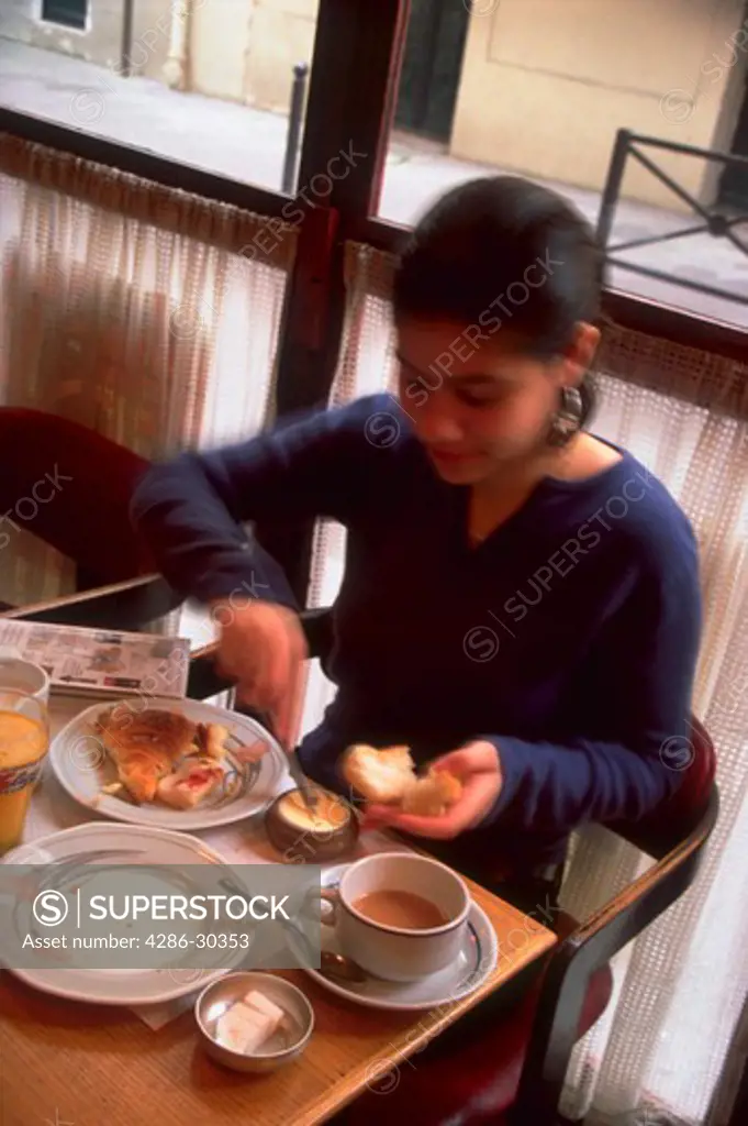 Blurred image of a woman sitting in a cafe eating breakfast, Paris, France.