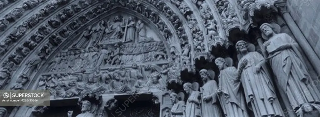Black and white image of the statues and ornate design of the front exterior of the Notre Dame Cathedral, Paris, France.