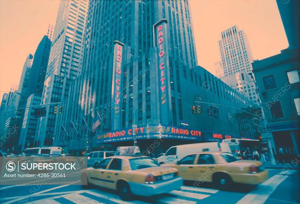 Taxis and vans pass through the intersection of Sixth Ave. & 50th St. in front of Radio City Music Hall, New York City.