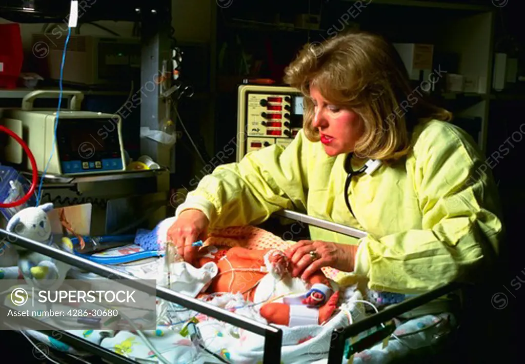 Neonatologist cares for infant in hospital neo-natal intensive care unit (NICU).