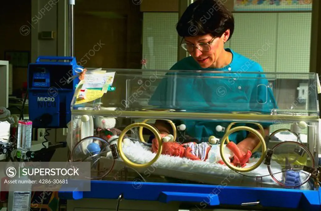 Registered nurse cares for premature infant in hospital neo-natal intensive care unit (NICU).