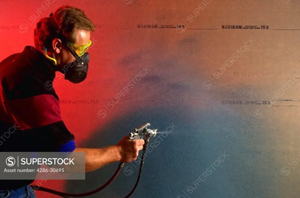 Masked worker operates paint/glue sprayer.