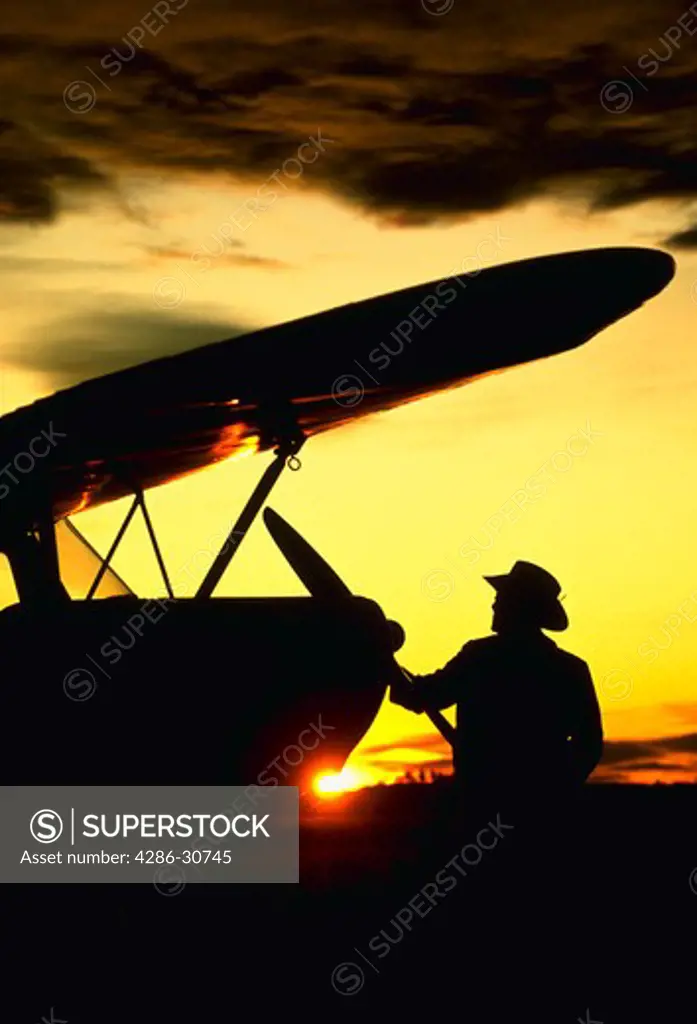 Pilot inspects airplane at sunset.