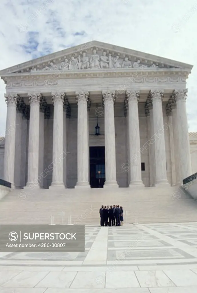 A cluster of lawyers stand before the front steps of the U.S. Supreme Court building, Washington, DC.