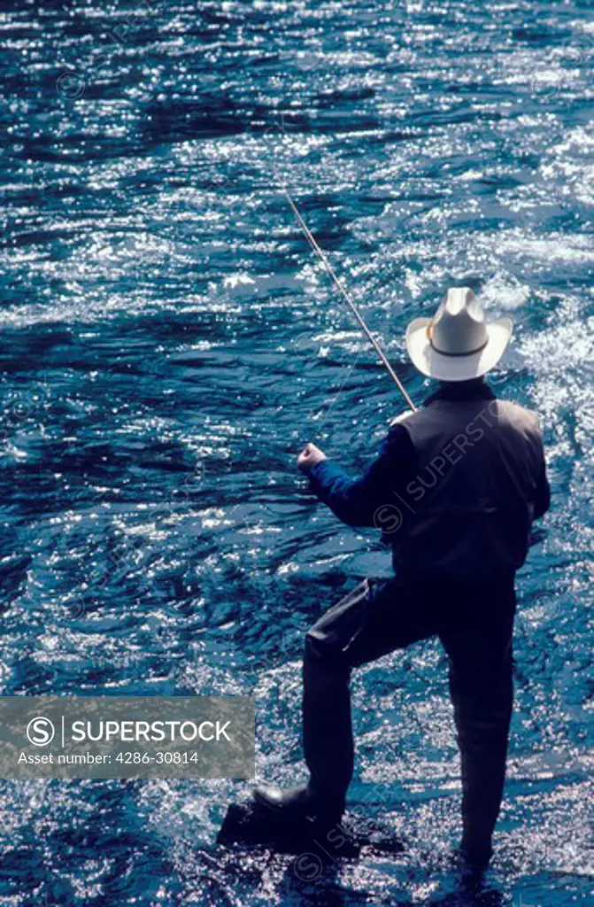 A sport fisherman stands on rock while fishing in a swiftly moving stream. 