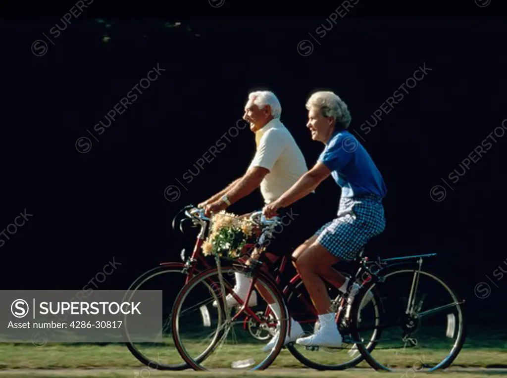 Senior couple riding bicycles together outdoors.