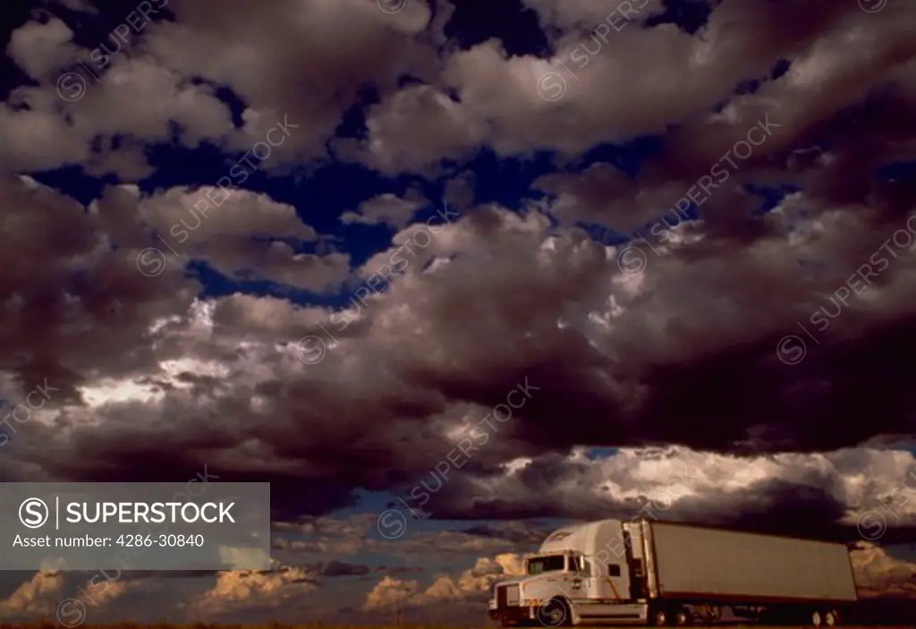 Truck traveling on interstate highway under dark storm clouds in Wyoming.