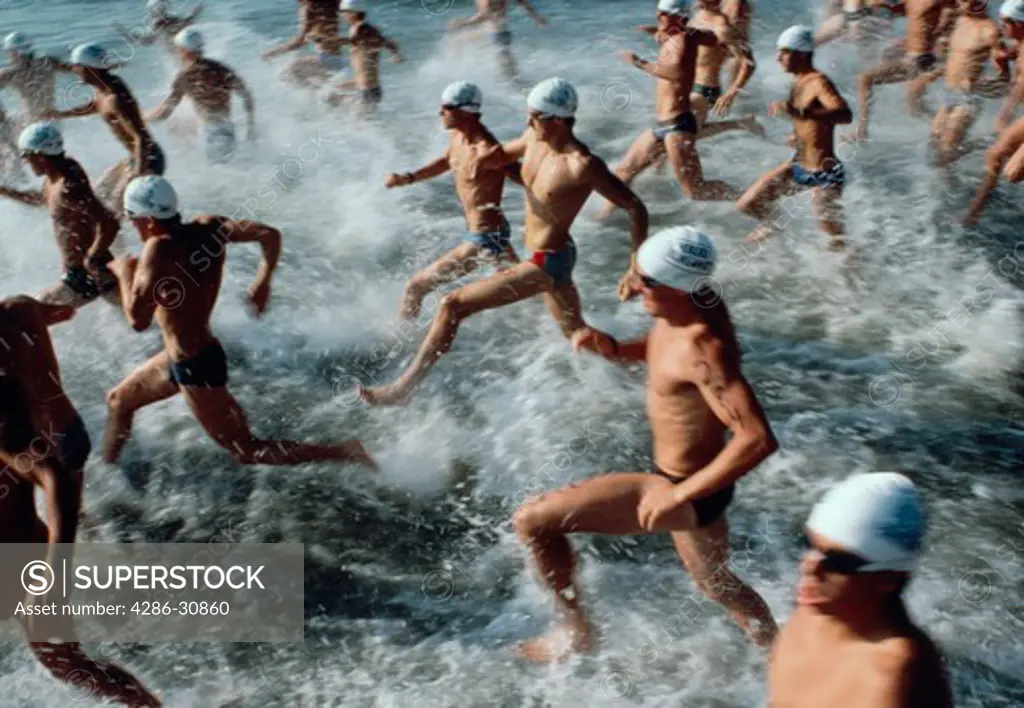 Group of athletes running into the ocean for the swimming portion of a triathalon.