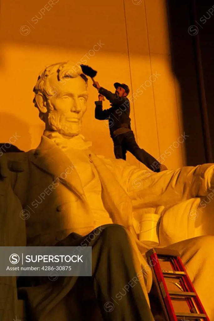 Custodian uses a broom to clean the head of the statue of Abraham Lincoln in morning light, Lincoln Memorial, Washington, DC 