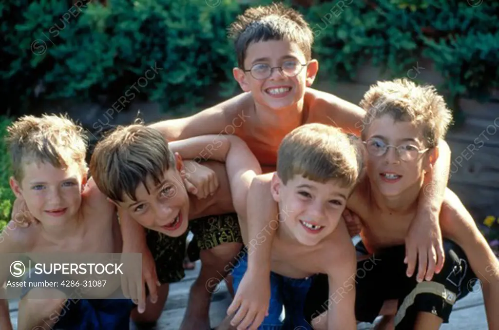 Portrait of five young boys in swimsuits clowning together at the pool.