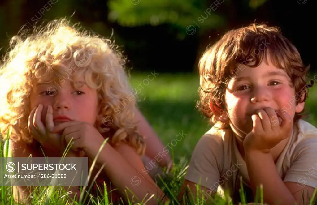 Portrait of a young blond girl and her brother lying on the grass.