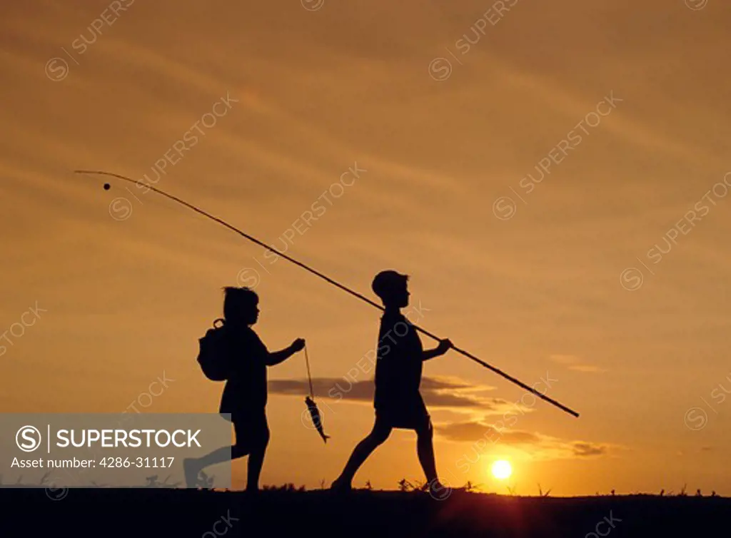 Silhouette of a young boy and girl walking home at the end of the day after they had gone fishing.