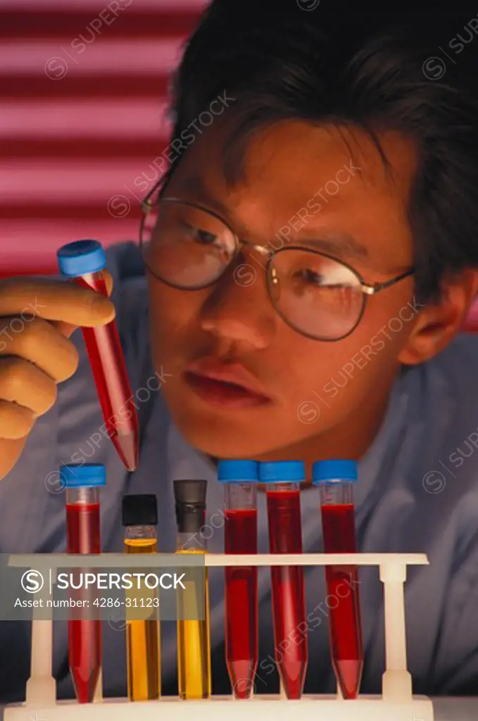 Close-up of an Asian male laboratory technician inspecting vials of samples in test tubes. 