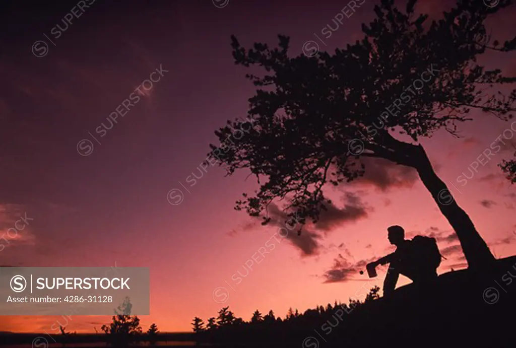 Silhouette of a backpacker sitting and resting on a cliff next to a tree in northern Minnesota. 