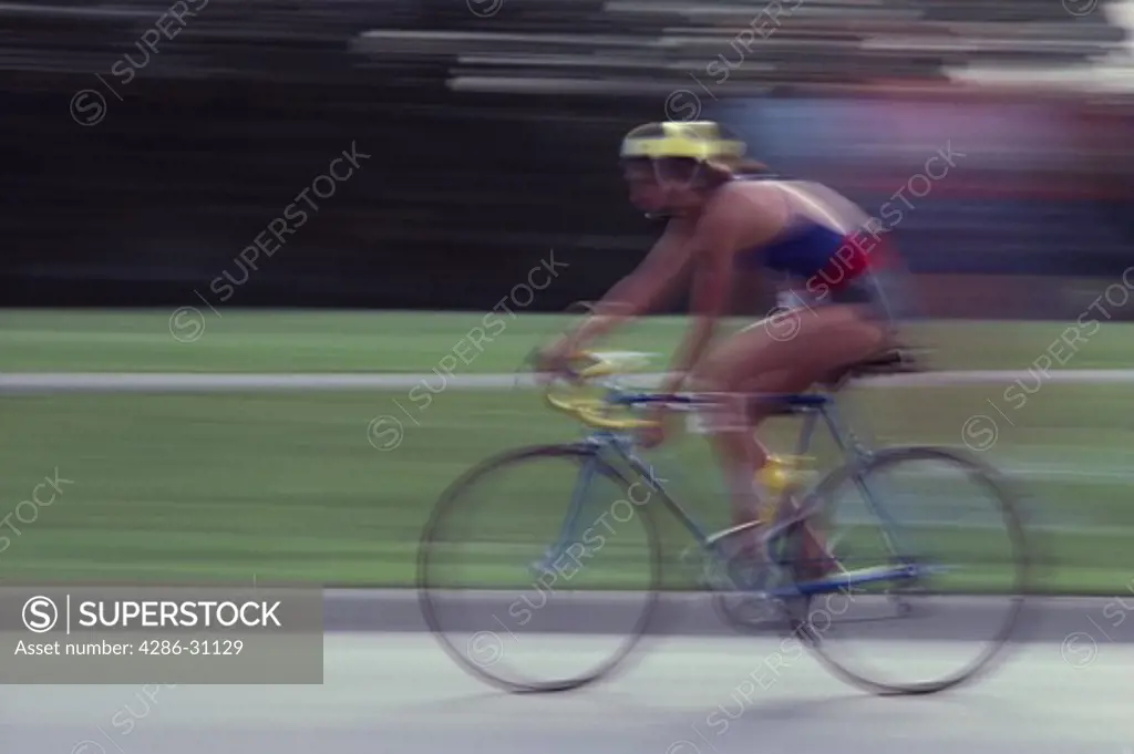 Blurred image of a female bicyclist participating in a triathlon race. 
