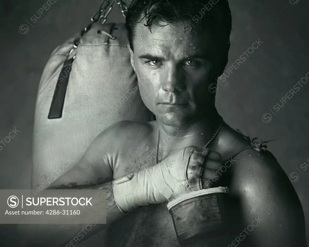 Portrait of a perspiring male boxer with boxing gloves, hands taped and punching bag.