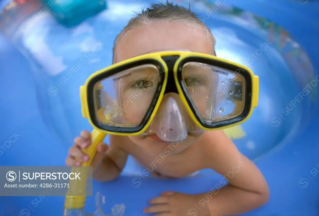 Young boy in swimming pool wearing snorkeling mask that is too big for his face.