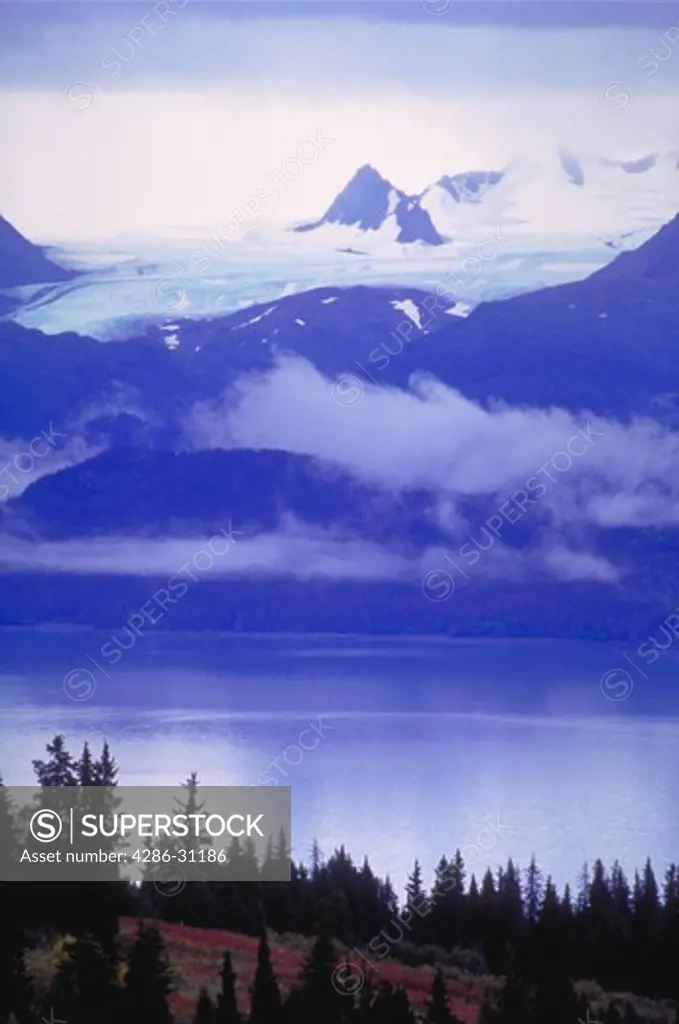 View looking down at the snow covered mountains and clouds reflected in the water of peaceful Kachemak Bay on Alaskas Kenai Peninsula.