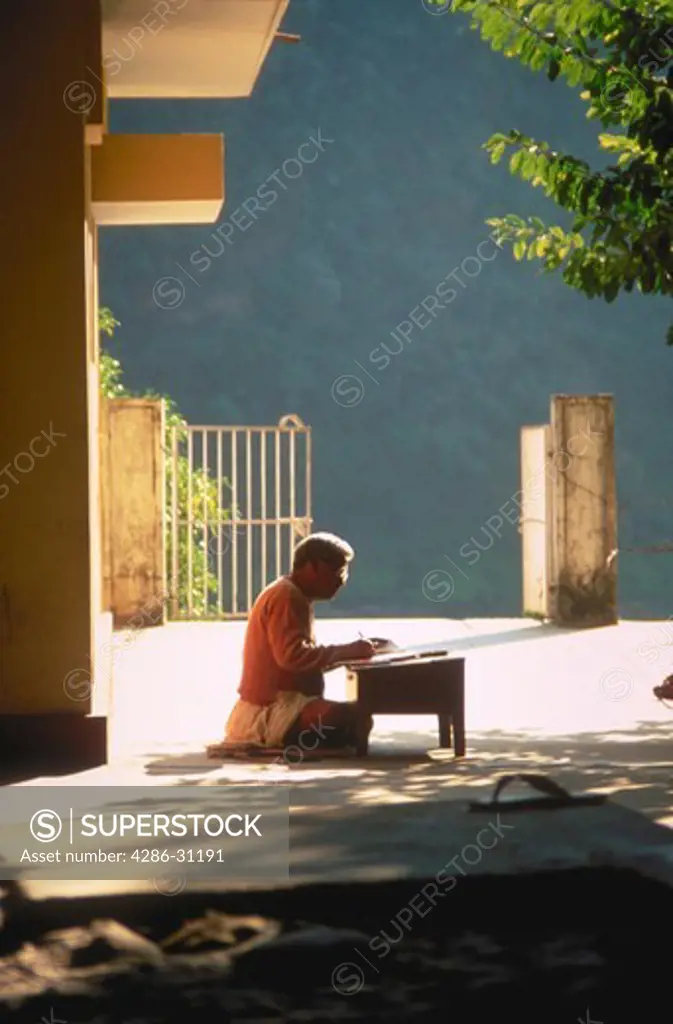 A Hindu priest sitting on the floor writing near Hardiwar in Northern India.