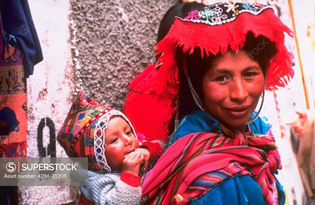 A woman wearing colorful clothing carrying a child on her back at Pisac market near Ollantaytambo, Peru.
