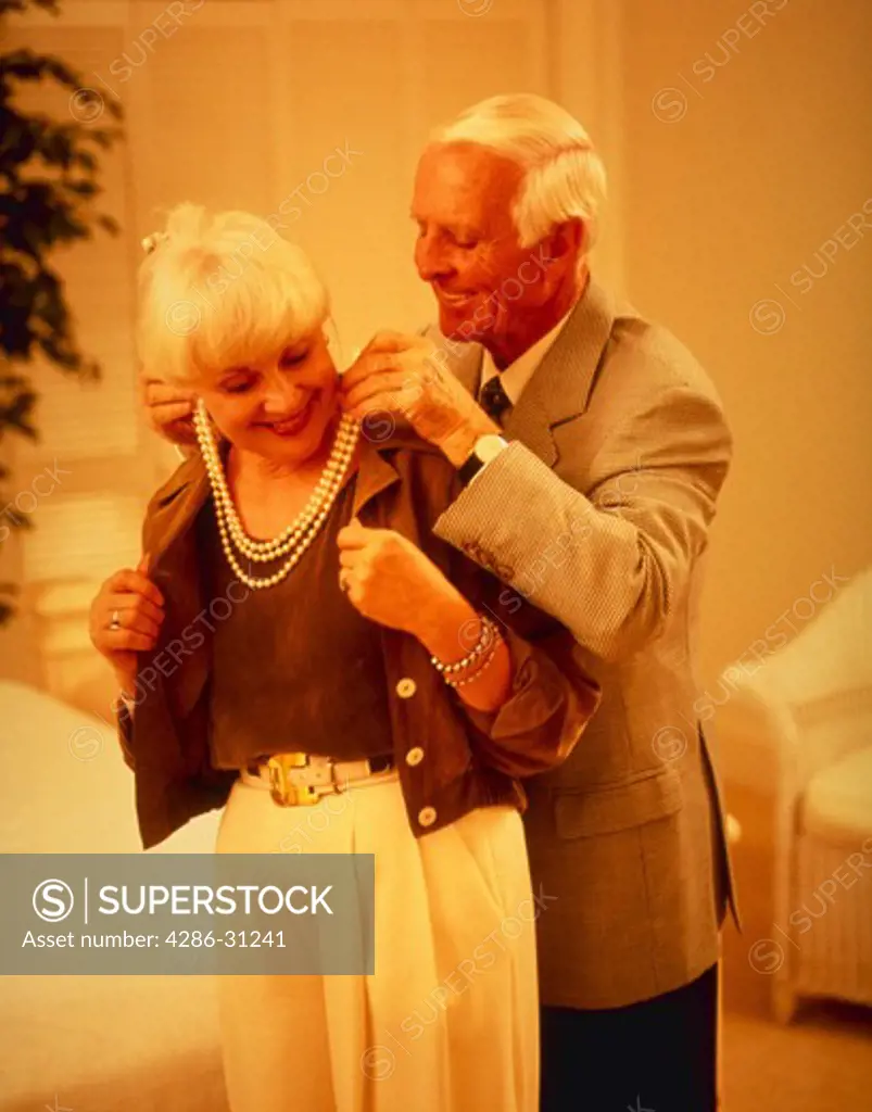 Senior man helps wife put on necklace.