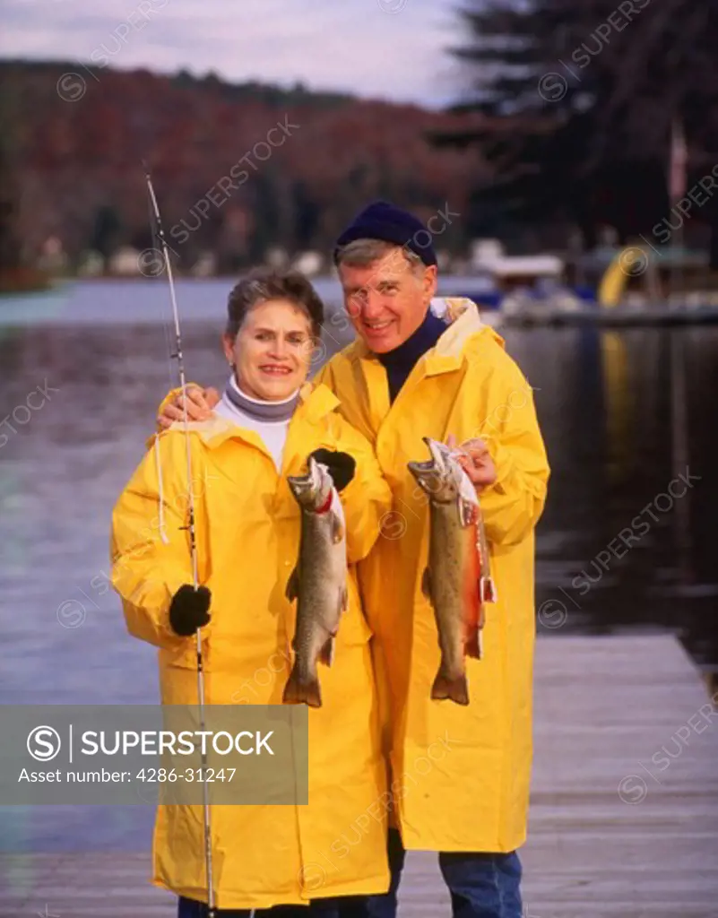 Couple in rain slickers holding catch after fishing.