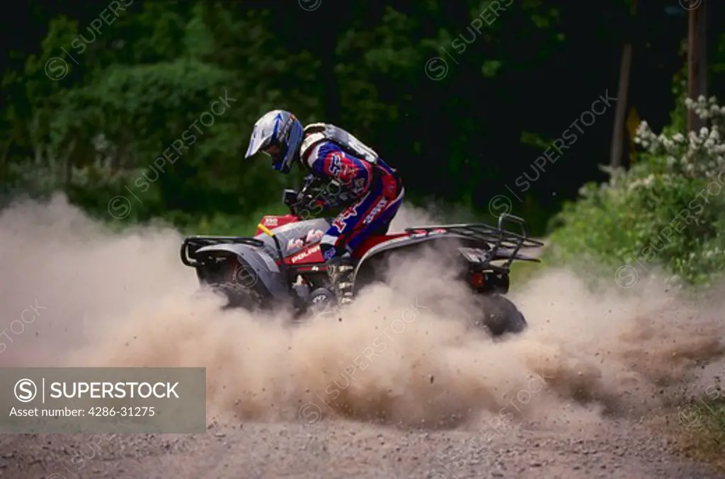 Man riding an all-terrain recreational vehicle and kicking up dust as he goes around a turn.