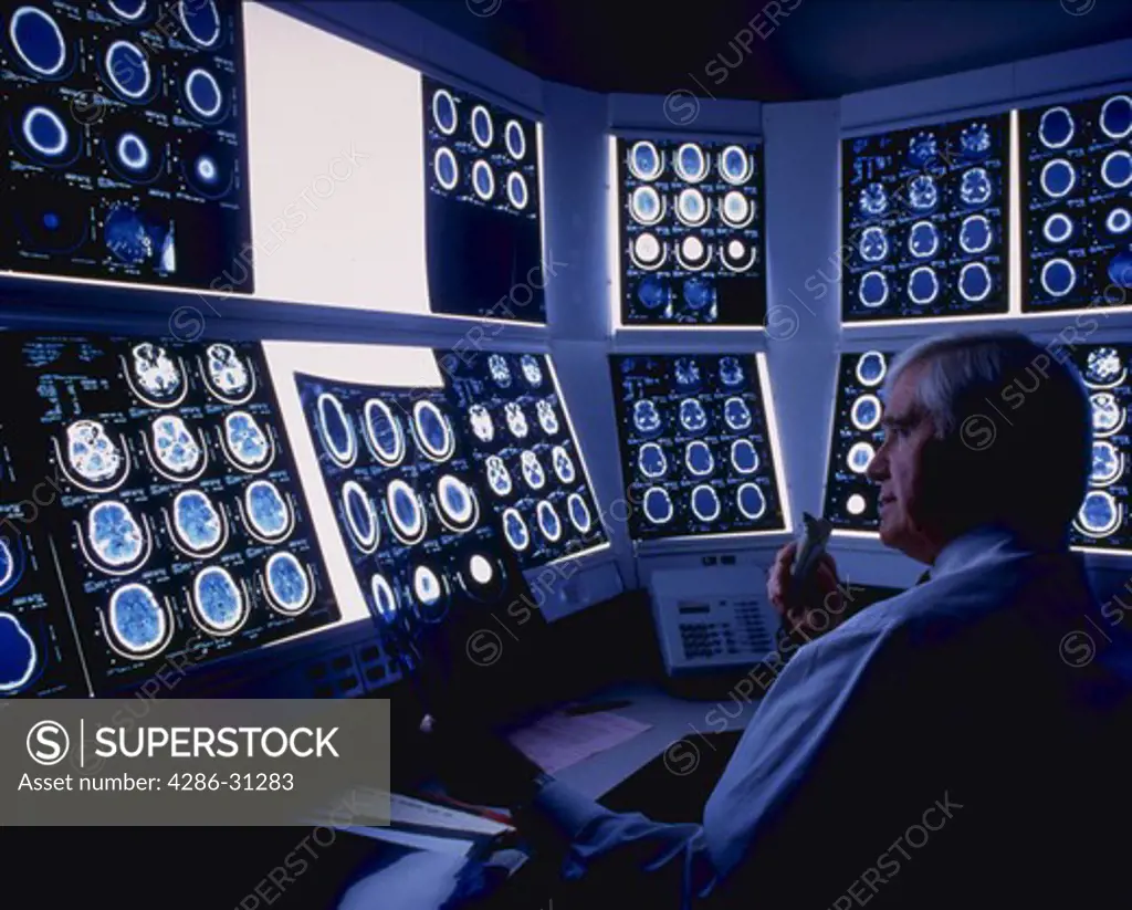 Senior doctor dictating notes into tape recorder while looking at x-rays on light boxes.