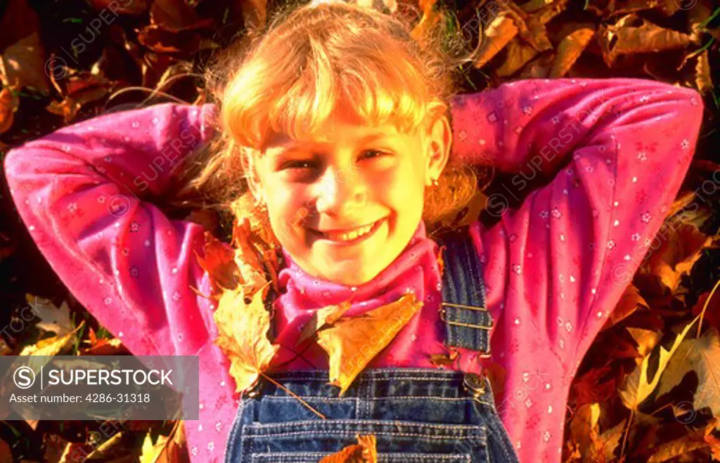 Portrait of a young blond girl lying in a pile of fall leaves.